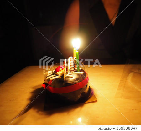 Cake candle birthday dessert chocolate celebration glow on small chocolate cake in dark room creating intimate festive mood Cake candle birthday dessert chocolate celebration glow on small chocolate cake in dark room creating intimate festive mood 139538047