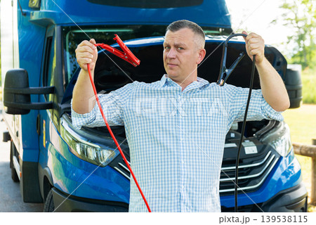 Driver showing jumper cables near blue delivery truck 139538115