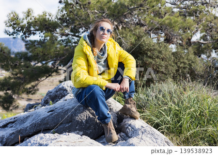 Woman in yellow jacket sitting on rock in pine forest Woman in yellow jacket sitting on rock in pine forest 139538923