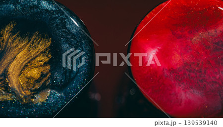 Glitter sphere. Fluid splatter. Defocused pink blue golden splash symmetrical ink liquid floating on abstract red maroon bokeh background. 139539140