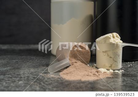 Vanilla and chocolate whey protein powder in scoops, food supplements, dark background, copy space 139539523