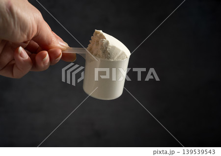 Vanilla whey protein powder in scoop, food supplements, female hand holding protein powder Vanilla whey protein powder in scoop, food supplements, female hand holding protein powder 139539543