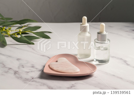 Rose quartz gua sha tool and oil bottles, face massage tool, beauty abstract photo Rose quartz gua sha tool and oil bottles, face massage tool, beauty abstract photo 139539561