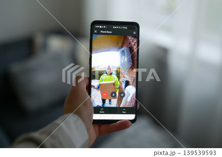 Closeup of a woman using a smartphone app to watch a delivery man dropping off a package Closeup of a woman using a smartphone app to watch a delivery man dropping off a package 139539593