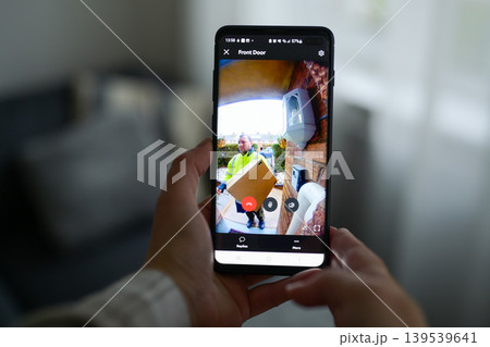 Closeup of a woman using a smartphone app to watch a delivery man dropping off a package Closeup of a woman using a smartphone app to watch a delivery man dropping off a package 139539641