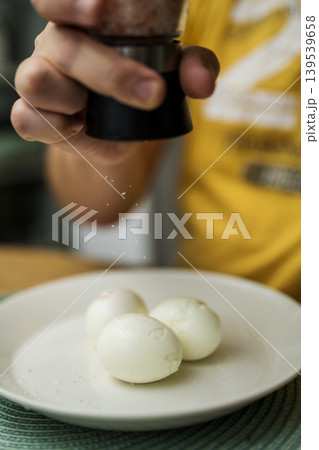 Boiled eggs for breakfast. Man's hand salting three boiled eggs in a plate. Eating proteins Boiled eggs for breakfast. Man's hand salting three boiled eggs in a plate. Eating proteins 139539658