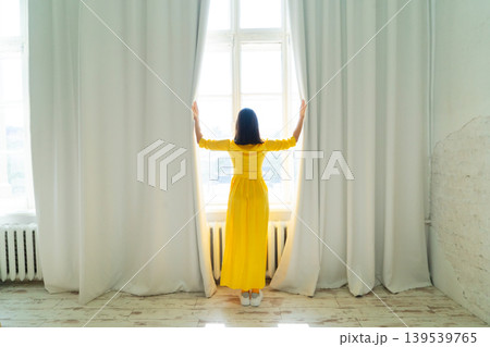 A Cheerful Woman Dressed in a Vibrant Yellow Dress is Posing Gracefully and Happily Near the Bright Window A Cheerful Woman Dressed in a Vibrant Yellow Dress is Posing Gracefully and Happily Near the Bright Window 139539765
