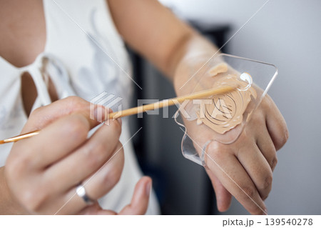 Female makeup artist applying foundation on hand using a spatula, showcasing skin tone matching techniques and beauty application methods in a bright studio environment Female makeup artist applying foundation on hand using a spatula, showcasing skin tone matching techniques and beauty application methods in a bright studio environment 139540278