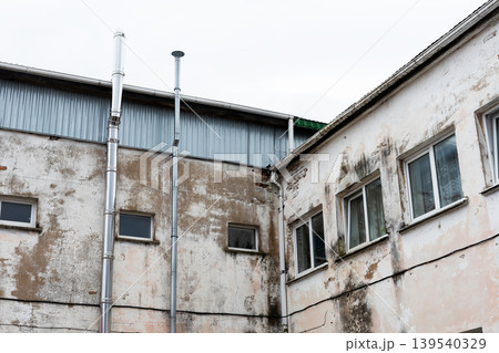 Abandoned factory with weathered exterior. Dilapidated industrial structure under gloomy sky Abandoned factory with weathered exterior. Dilapidated industrial structure under gloomy sky 139540329