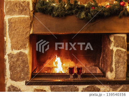 Two glasses with mulled wine are near the fireplace. Christmas decorations and cups with a spicy hot drink. Open fire and stone walls. New Year Eve. 139540356