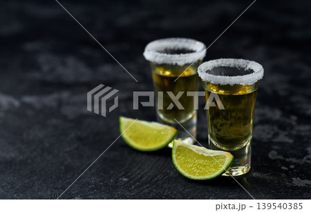 Two shot of golden tequila with white salt crystals and lime on a dark table,  selective focus. 139540385