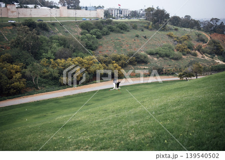 Scenic view of a couple in formal attire walking hand in hand on a grassy hillside, surrounded by lush greenery and a winding path, capturing a romantic outdoor moment Scenic view of a couple in formal attire walking hand in hand on a grassy hillside, surrounded by lush greenery and a winding path, capturing a romantic outdoor moment 139540502