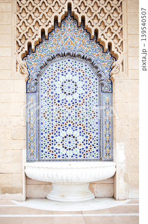 Ornate tile fountain with intricate geometric patterns and vibrant colors, set against a textured stone wall, showcasing traditional craftsmanship and architectural beauty Ornate tile fountain with intricate geometric patterns and vibrant colors, set against a textured stone wall, showcasing traditional craftsmanship and architectural beauty 139540507