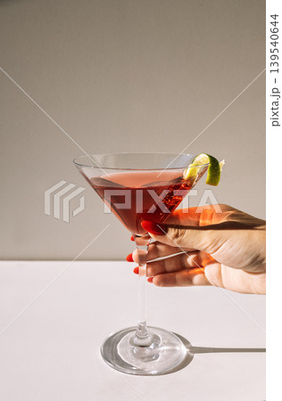 Close-up of a martini glass and a female hand with a red manicure 139540644