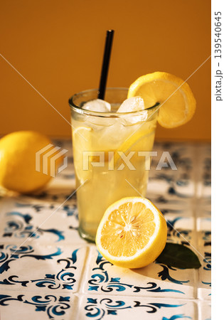 Close-up of a glass of delicious lemonade with ice cubes on a table made of white tiles with blue patterns 139540645