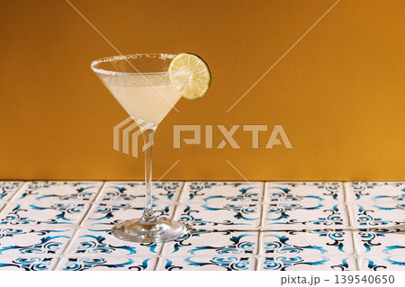 Close-up of an elegant margarita cocktail glass with a slice of lime and sugar on a yellow background. Close-up of an elegant margarita cocktail glass with a slice of lime and sugar on a yellow background. 139540650