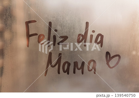 Handwritten Portuguese wish Feliz dia Mama is Happy Mother's Day in English on misted glass on sunset rainy window 139540750