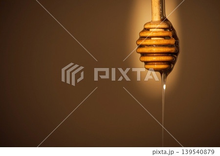 Honey dipper dripping golden honey against a soft brown background, showcasing the texture and color of the honey in a close-up shot Honey dipper dripping golden honey against a soft brown background, showcasing the texture and color of the honey in a close-up shot 139540879