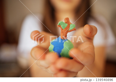 Child holding a small globe made of clay with a tree on top, showcasing a creative representation of Earth and nature in a close-up view 139540896