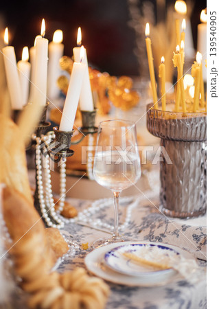 Elegant dining table set for a festive occasion with lit candles, glass of water, decorative bread, and intricate tableware arranged for a special gathering 139540905