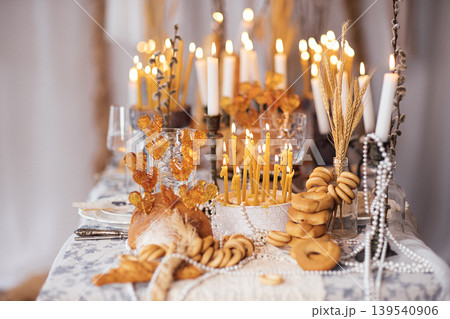 Festive dining table set with candles, decorative elements, and assorted baked goods for a celebration, featuring golden hues and elegant glassware in a cozy indoor setting 139540906
