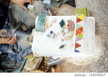 Skilled artisan working on colorful mosaic pieces, surrounded by tools and materials, showcasing craftsmanship and creativity in a vibrant workshop environment 139540937
