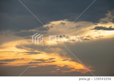 Warm sunset light breaks through layered clouds, creating a dramatic sky with soft golden tones and moody atmosphere, perfect for backgrounds, nature themes, and peaceful evening concepts. 139541056