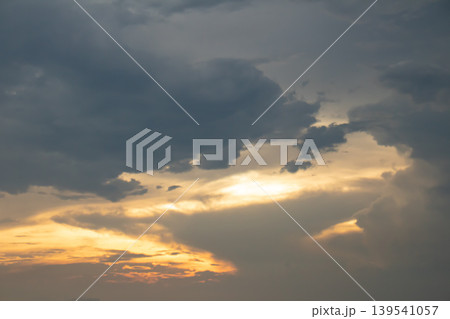 Dark clouds drift across a glowing evening sky as warm sunlight breaks through, creating a dramatic contrast of light and shadow, ideal for atmospheric backgrounds and nature concepts. 139541057