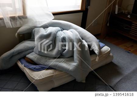 薄暗い部屋で布団や枕を雑に片付けた朝。ベッドの上に積み重ねられた寝具 薄暗い部屋で布団や枕を雑に片付けた朝。ベッドの上に積み重ねられた寝具 139541618