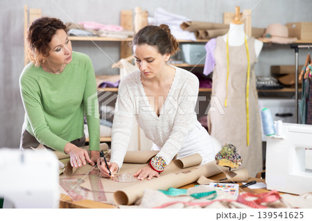 Female seamstresses drafting clothing pattern on paper in sewing workshop Female seamstresses drafting clothing pattern on paper in sewing workshop 139541625