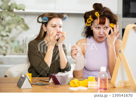Female friends applying sheet masks to faces by vanity mirror 139541670