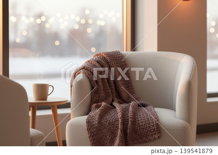 Cozy armchair with a warm blanket and steaming mug by a window Cozy armchair with a warm blanket and steaming mug by a window 139541879