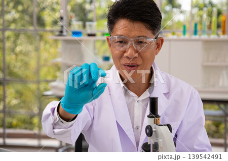 Scientist holding medical capsule in laboratory research environment with microscope and scientific equipment, pharmaceutical innovation and healthcare technology concept 139542491