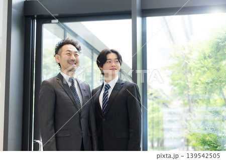 新緑のオフィスの窓際で見上げる若手ビジネスマンと上司 139542505