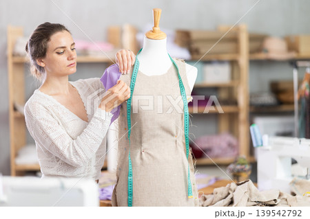 Female tailor sews new dress on a mannequin in sewing studio 139542792