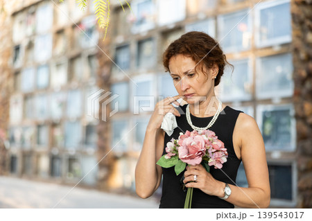 Upset woman in black dress, who lost loved one, brings flowers to grave Upset woman in black dress, who lost loved one, brings flowers to grave 139543017