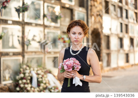Woman in black mourning dress standing with flowers near columbarium Woman in black mourning dress standing with flowers near columbarium 139543036