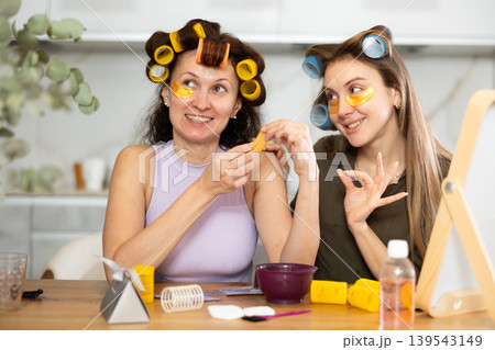 Female friends in colorful rollers applying golden under-eye patches Female friends in colorful rollers applying golden under-eye patches 139543149