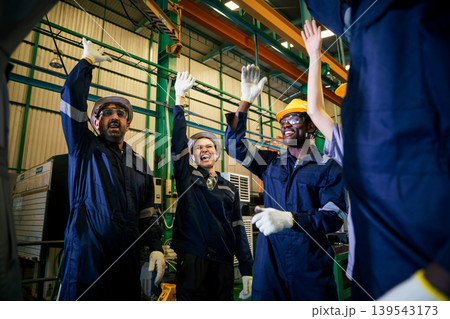 Factory workers celebrating success with raised hands in workshop Factory workers celebrating success with raised hands in workshop 139543173