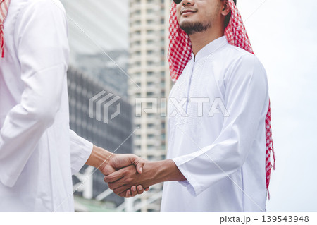 Islamic businessman shake hands together dealing success business in modern muslim UAE city. Arab man wear hijab muslim dress. Multicultural diversity business people meeting talking group cityscape 139543948