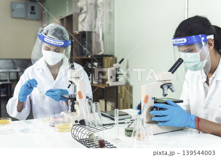 Scientist man woman working together team partner look into Microscope research in science laboratory. Two Asian scientist use microbiology microscope chemistry lab equipment. Biochemistry researcher 139544003