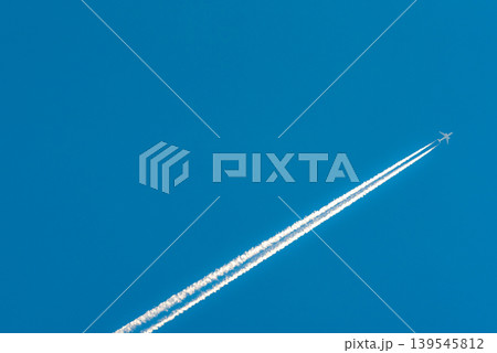 Airplane with white condensation tracks. Jet plane on clear blue sky with vapor trail. Travel by aeroplane concept. Trails of exhaust gas from airplane engine. Aircraft with white stripes. 139545812
