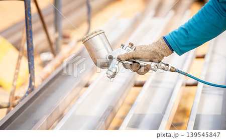 Construction worker painting metal structure surface coating with a spray gun at construction site. Metal corrosion and rust protection. Industrial precision. Protective coating to a metal structure. Construction worker painting metal structure surface coating with a spray gun at construction site. Metal corrosion and rust protection. Industrial precision. Protective coating to a metal structure. 139545847