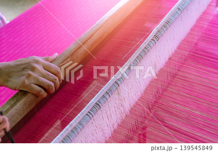 Woman working on weaving machine for weave handmade fabric. Textile weaving. Weaving using traditional hand weaving loom on the long cotton strands. Textile production in Thailand. Asian culture. Woman working on weaving machine for weave handmade fabric. Textile weaving. Weaving using traditional hand weaving loom on the long cotton strands. Textile production in Thailand. Asian culture. 139545849