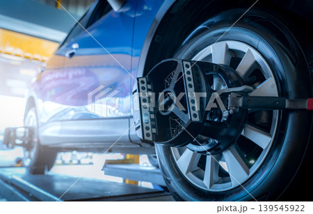 Wheel alignment equipment grip the tire of car wheel in car repair shop. Auto wheel alignment in workshop of service station. Car wheel balance. Suspension adjustment. Vehicle inside garage workshop. 139545922