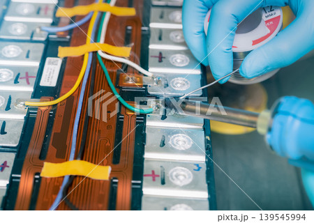 Technician use soldering iron to solder metal and wire of lithium-ion rechargeable battery. Repair module of Li-ion battery. Engineer hand holds soldering iron and tin-lead to solder electronic board. 139545994