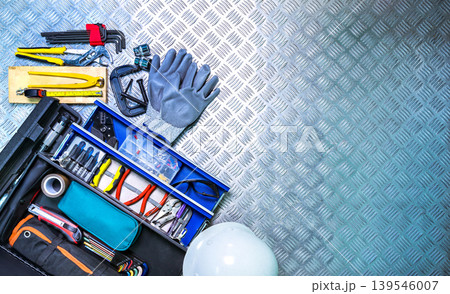 Top view toolbox and safety helmet on checkered plate background in workshop, service tools set for construction electrical and plumbing repair, concept of technician equipment, maintenance work. 139546007