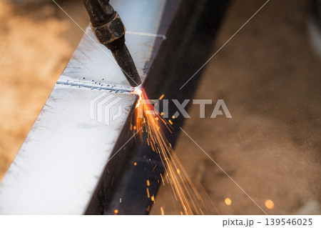Skilled welder cuts metal with a gas torch in industrial workshop. Sparks fly during precision fabrication process. Craftsman control and expertise in metalworking. Gas torch cuts through steel. Skilled welder cuts metal with a gas torch in industrial workshop. Sparks fly during precision fabrication process. Craftsman control and expertise in metalworking. Gas torch cuts through steel. 139546025