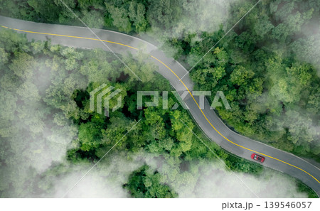 Aerial top view of a red car driving on highway road in green forest. Sustainable transport. Electric vehicle driving on asphalt road through lush green forest. Zero emission car. Green mobility. Aerial top view of a red car driving on highway road in green forest. Sustainable transport. Electric vehicle driving on asphalt road through lush green forest. Zero emission car. Green mobility. 139546057