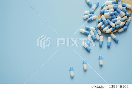 Blue and white antibiotic capsule pill and wooden spoon on blue background. Pills frame with space. Antibiotic drugs. Pharmaceutical industry. Pharmacology. Healthcare and medical care concept. Blue and white antibiotic capsule pill and wooden spoon on blue background. Pills frame with space. Antibiotic drugs. Pharmaceutical industry. Pharmacology. Healthcare and medical care concept. 139546102